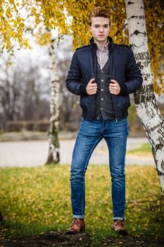 Fall season and people concept. Full length of young stylish fashionable man posing against autumn birch trees. Yellow leaves background