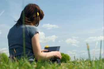 Woman typing on a laptop outside in a meadow. Blue sky with clouds.