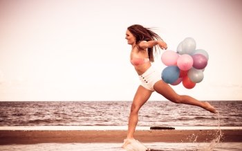 Summer holidays, celebration and lifestyle concept - attractive athletic woman teen girl jumping with colorful balloons outside on beach, aged retro tone