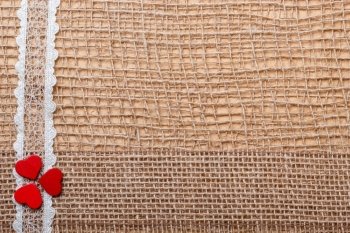 Valentines day or wedding concept. Red wooden decorative hearts lace ribbon on abstract cloth burlap background with copy space