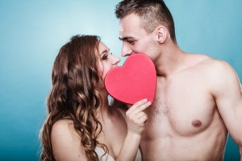 Attractive young couple kissing behind red heart against blue background