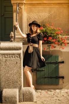 Portrait of young romantic woman outdoors. Retro styling fashion girl in black hat and dress on street of the old town city Gdansk Danzig Poland