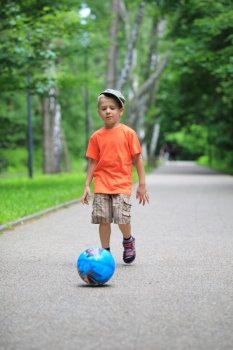 Boy young kid playing with ball kicks running towards ball in park outdoors