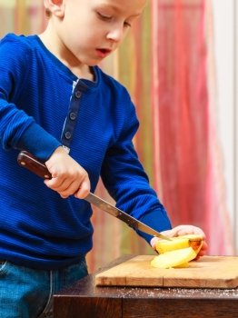 Child little boy playing dangerous game with a kitchen knife cut apple, making salad at home.