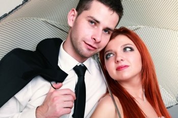 Wedding day. Portrait of happy married couple red haired blue eyed bride and groom with umbrella studio shot on gray background