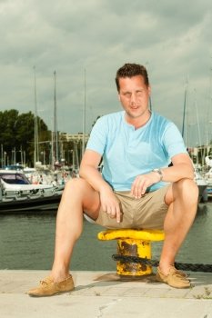 Travel tourism vacation and people concept. Fashion portrait of handsome man on pier against white yachts in port