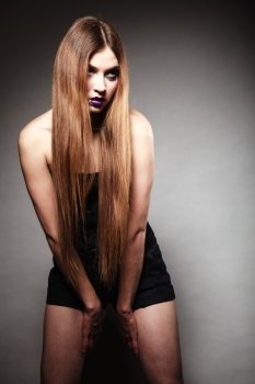 Sad young woman with long hair and creative makeup. Unhappy girl in gothic style on dark background. Negative emotions. Studio shot.