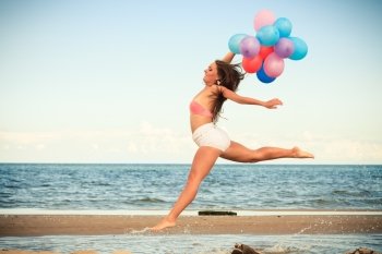 Summer holidays, celebration and lifestyle concept - attractive athletic woman teen girl jumping with colorful balloons outside on beach, sunny day
