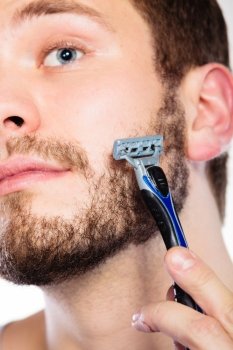 Health beauty and skin care concept. Closeup of male face. Young man guy styling beard holding disposable blue razor blade.