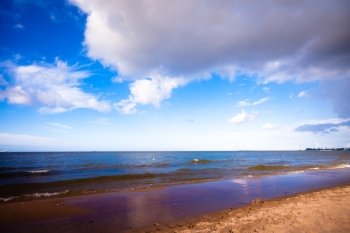 Landscape. View of blue cloudy sky at sea or ocean water with footprints at sandy beach. Resort.