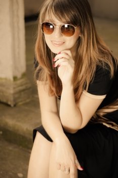 Portrait of young woman outdoors. Retro style fashionable girl in black classic dress and sunglasses relaxing on street of the old town city Gdansk Danzig Poland