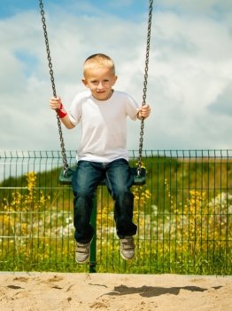 Little blonde boy having fun at the playground. Child kid playing on a swing outdoor. Happy active childhood.