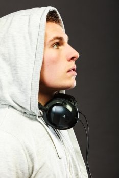 Closeup young handsome hooded man with headphones listening to music sideview dark background