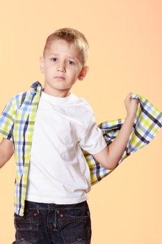 little serious blonde boy child trying on shirt orange background