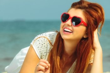 Holidays, vacation travel and freedom concept. Beautiful redhaired happy girl in heart shaped sunglasses on beach.