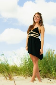Smiling happy woman on beach. Young model in black dress outside.