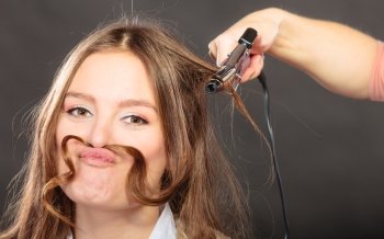 Stylist curling for pretty woman. Girl with hair mustache care about her hairstyle.