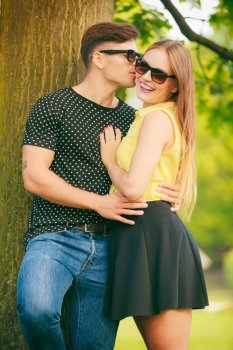 Love and happiness. Young happy couple lovers wearing sunglasses dating in summer park outdoor. Man whisper taking to woman ear.