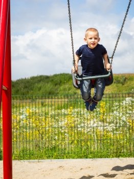 Little blonde boy having fun at the playground. Child kid playing on swing outdoor. Happy active childhood.