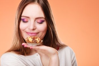 Bakery sweet food and people concept. Content attractive woman closed eyes holds cake cupcake in hand smelling orange background