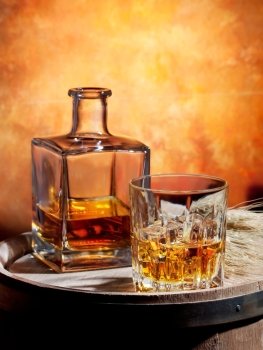 Bottle and glass of whiskey with ice on a wooden barrel