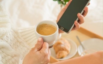 Woman eating breakfast in bed while looking at your mobile phone